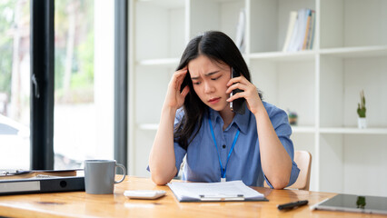 A stressed Asian businesswoman is feeling overwhelmed, trying to fix the problems over the phone