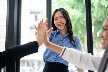 A cheerful Asian businesswoman is putting her hand up or giving high fives to her team