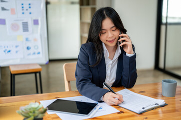 A professional Asian businesswoman is making a call to her client, working at her desk