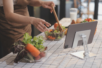 Delicious fruit and vegetables on a table and woman cooking. Housewife is cutting green cucumbers on a wooden board for making fresh salad in the kitchen.