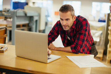 Middle aged caucasian man working on a laptop in a printing press office