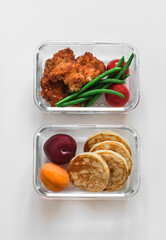 School lunch box - containers with nuggets, green beans, pancakes and fruit on a light background, top view