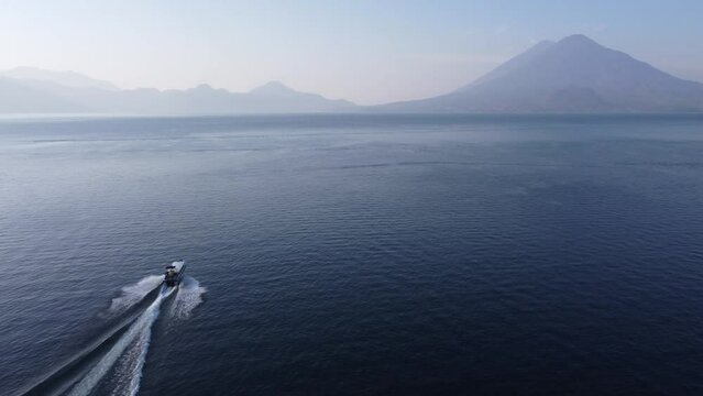 Aerial follows tourism tour boat on Lake Atitlan, GTM volcano mountain