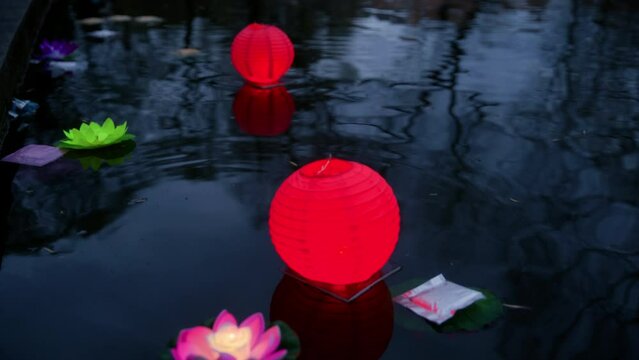 Cropped image of woman keeping paper lantern on water. Artificial glowing flowers floating in river. She is celebrating traditional festival during night.
