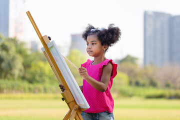 Happy child girl drawing a picture outdoors, Kid girl painting on canvas in the garden