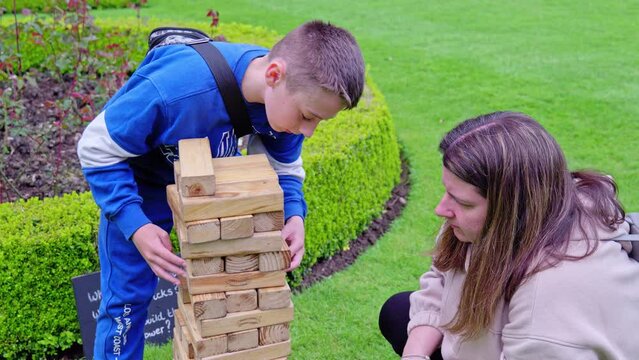 Young boy and mother playing a wooden block building game, set in a country garden outdoors.