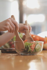 Delicious fruit and vegetables on a table and woman cooking. Housewife is cutting green cucumbers on a wooden board for making fresh salad in the kitchen.