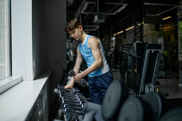 Teenager boy taking dumbbell of different weights from gym rack
