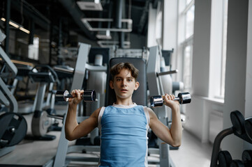 Portrait of strong fitness boy training with dumbbells at gym