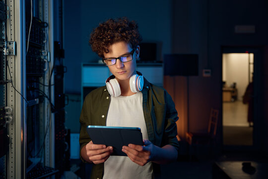 Teenager guy IT technician working on tablet in server room - Powered by Adobe