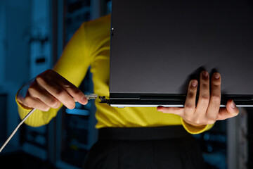 Closeup woman connecting internet network cable to laptop in server room