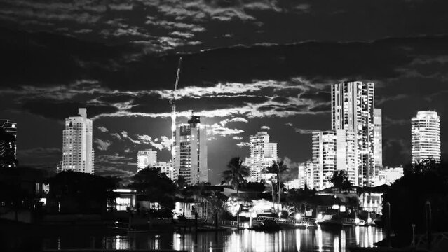 Time lapse of a sunset scene at Broadbeach canal, with skyscrapers in the background and boats passing by in grey color.