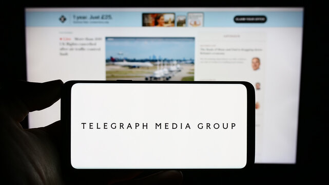 Stuttgart, Germany - 08-28-2023: Person holding mobile phone with logo of company Telegraph Media Group Limited (TMG) on screen in front of web page. Focus on phone display.