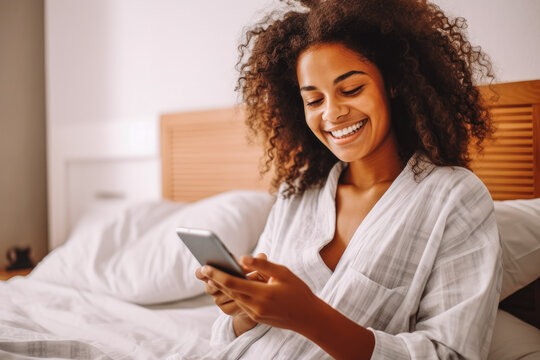 Cheerful black woman resting in bed while scrolling on her phone.