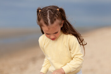 A little girl in a yellow sweater runs along the sandy beach. Blurred sea background. Happy vacation days