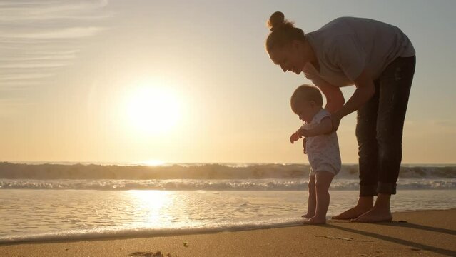 Mom exploring her baby to the world around him. Caring mother and her toddler child in nature in summer by sea. Happy motherhood concept. Happy mother and child on the sandy beach on summer vacation