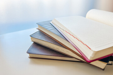 窓辺に積み上げられた古い日記帳と、まだ書かれていないページ