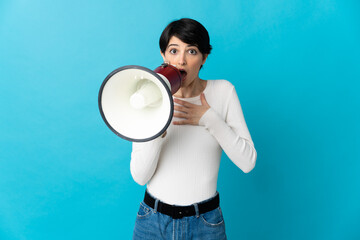 Woman with short hair isolated on blue background shouting through a megaphone with surprised expression