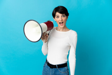 Woman with short hair isolated on blue background holding a megaphone and with surprise expression