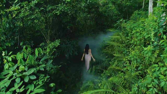 Drone shot of girl in pink dress running though a mist covered Rainforest path