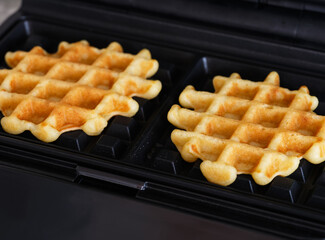 A close-up shot of a waffle maker with two gluten free homemade waffles inside of it.