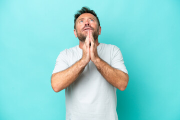 Middle age caucasian man isolated on blue background keeps palm together. Person asks for something