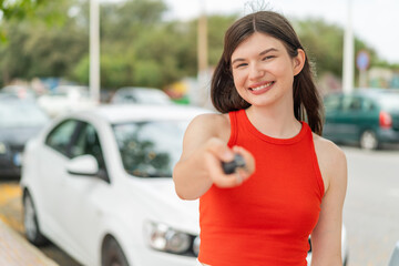 Young pretty woman at outdoors holding car keys with happy expression