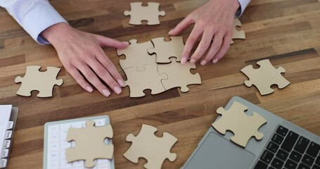 Woman collects beige puzzles sitting at wooden table at workplace in office. Concept of educational game and break at work slow motion