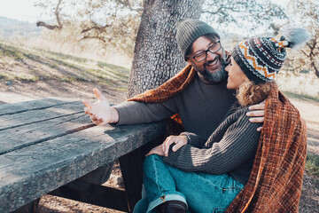 Happy adult couple enjoy time together in outdoor leisure activity sitting on a wooden bench and...