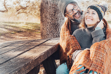 Adult couple have fun together with love and laughing sitting together on a bench in autumn season park. People enjoy outdoor leisure activity and laugh. Man hug woman smiling a lot. Relationship