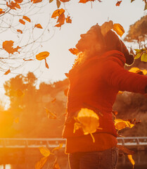 Winter is coming. Autumn sunset and happy woman throwing leaves in the air opening arms and smiling...