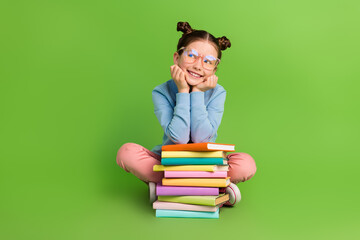Full body photo of minded dreamy cute little girl wear blue pullover sit with book look empty space isolated on green color background
