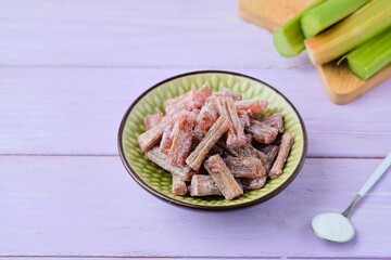 Candied rhubarb, sprinkled with powdered sugar, in a ceramic plate on a purple wooden background....