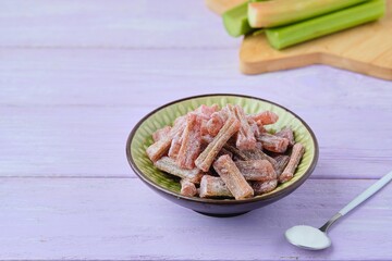 Candied rhubarb, sprinkled with powdered sugar, in a ceramic plate on a purple wooden background. Preparations, conservation. Rhubarb recipes.
