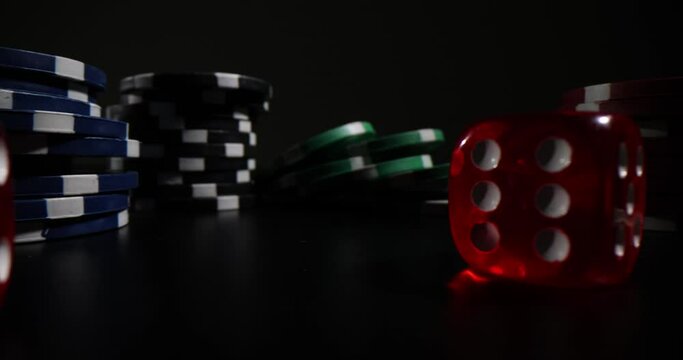 Multicolored bunch of casino chips and dices stands on black surface in dark premise. Professional accessories for playing gambling games concept