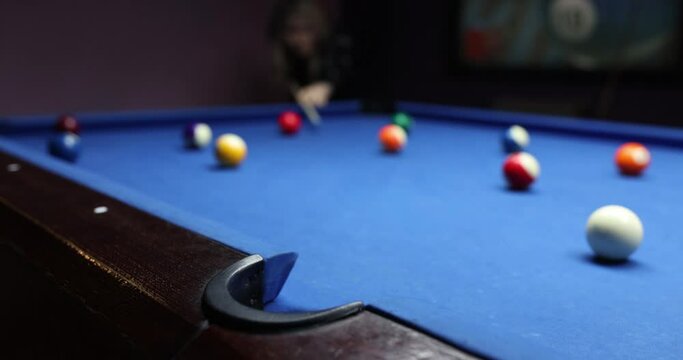 Player kicking coloured billiard balls on blue billiard pool table. People playing pool to pass leisure time in casino club slow motion