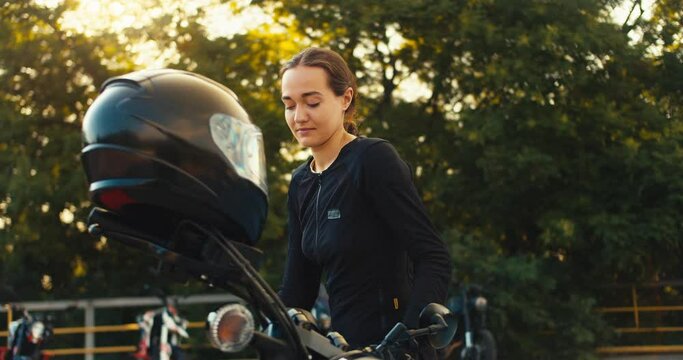 A girl gets behind the wheel of a motorcycle and puts on a helmet before her motorcycle driving training in a motorcycle school in sunny weather