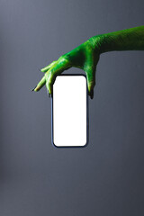 Vertical image of green monster hand holding smartphone with copy space on grey background © vectorfusionart