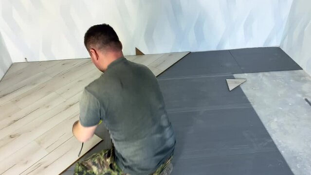 A hired worker marks the floor for laying the substrate under the laminate. A man lays wooden planks of laminate on the floor in a room of a new house. High quality 4k footage