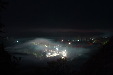 Naklejka na ściany i meble Mysterious cottage village in the middle of the valley at night in the fog