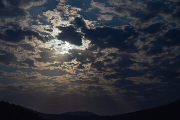 The moon shines through the clouds at night in the mountains