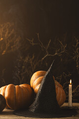 Fototapeta premium Vertical image of pumpkins and witch hat and burning candle with copy space on black background