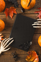 Fototapeta premium Vertical image of halloween decorations, skeleton hands on notebook, copy space on brown background