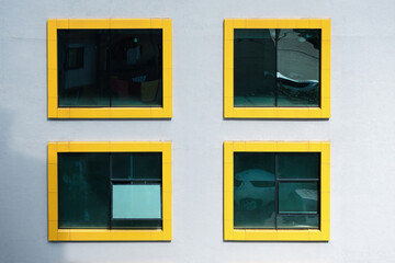 Four windows with yellow frames in a white color wall. Exterior of a building with yellow frame windows.