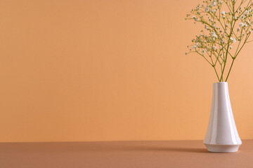 Fototapeta na wymiar White flowers in white vase and copy space on orange background