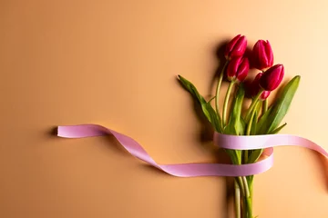 Zelfklevend Fotobehang Vertical image of bunch of red tulips with pink ribbon and copy space on orange background © vectorfusionart