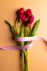 Fotobehang Vertical image of bunch of red tulips with pink ribbon and copy space on orange background © vectorfusionart
