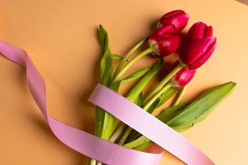 Stof per meter Bunch of red tulips with pink ribbon and copy space on orange background © vectorfusionart