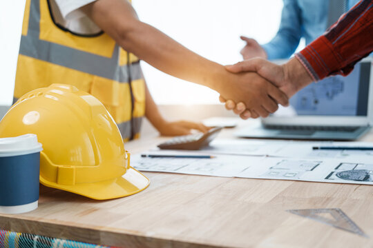 Shaking hands, interracial group of architects and engineers on meeting on blueprint for project work in, construction workers on a construction site