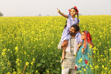 rural Indian family of a mother, father, and daughter standing in a mustard field and all of them are happy to see agricultural benefits of the field